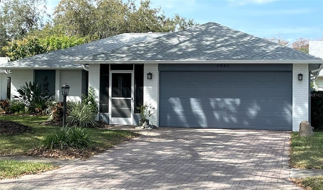 ranch-style home featuring a garage, decorative driveway, brick siding, and roof with shingles