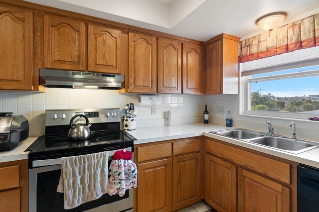 kitchen with under cabinet range hood, a sink, stainless steel range with electric cooktop, brown cabinets, and dishwasher