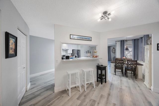 kitchen featuring stainless steel appliances, light wood-style floors, white cabinetry, a textured ceiling, and a kitchen bar