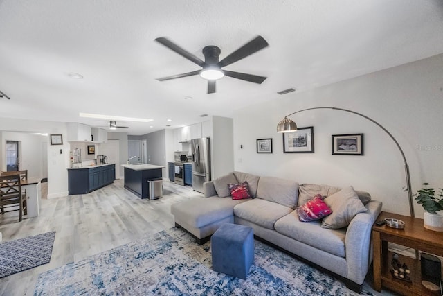 living area featuring a ceiling fan, light wood-type flooring, and visible vents