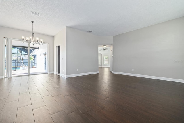 spare room featuring visible vents, dark wood-type flooring, ceiling fan with notable chandelier, a textured ceiling, and baseboards