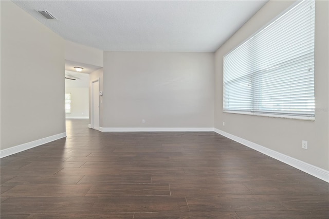 empty room with a textured ceiling, dark wood-style floors, visible vents, and baseboards