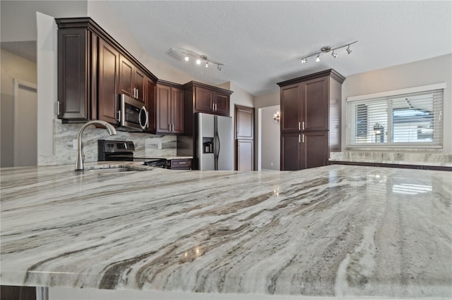 kitchen featuring light stone countertops, a sink, stainless steel appliances, a textured ceiling, and tasteful backsplash