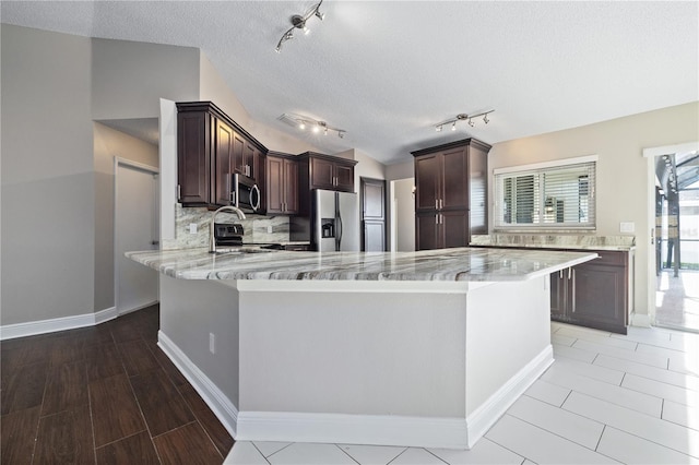 kitchen with a textured ceiling, stainless steel appliances, dark brown cabinetry, a peninsula, and decorative backsplash