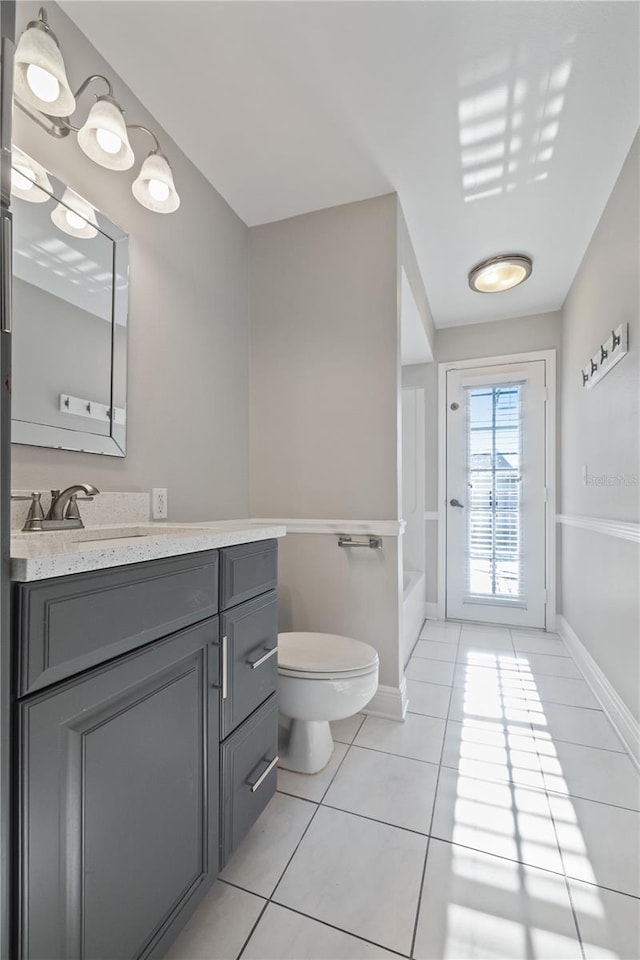 bathroom featuring tile patterned flooring, baseboards, toilet, a bathing tub, and vanity