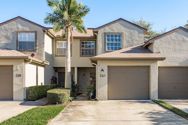 multi unit property with driveway, roof with shingles, an attached garage, and stucco siding