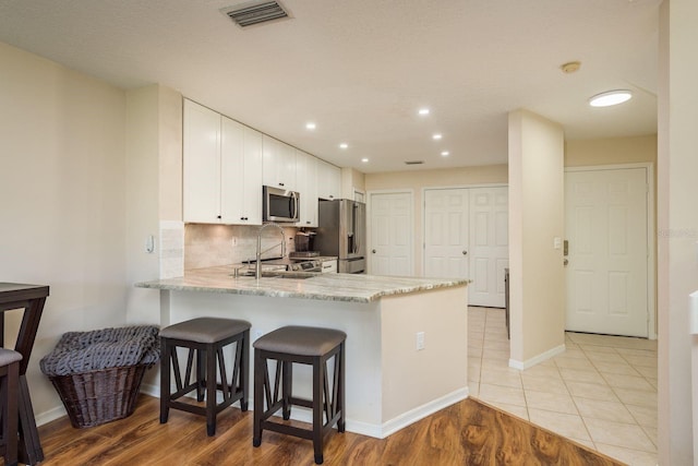 720 Earls Ct, Safety Harbor, FL 34695 - kitchen with stainless steel appliances, decorative backsplash, white cabinets, light stone countertops, and a peninsula