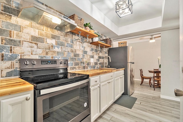 kitchen with under cabinet range hood, open shelves, wooden counters, and appliances with stainless steel finishes