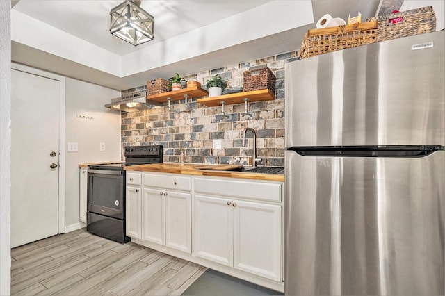 kitchen with butcher block countertops, range hood, freestanding refrigerator, electric range, and a sink