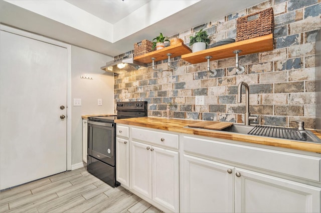 kitchen featuring electric range, butcher block countertops, open shelves, a sink, and ventilation hood