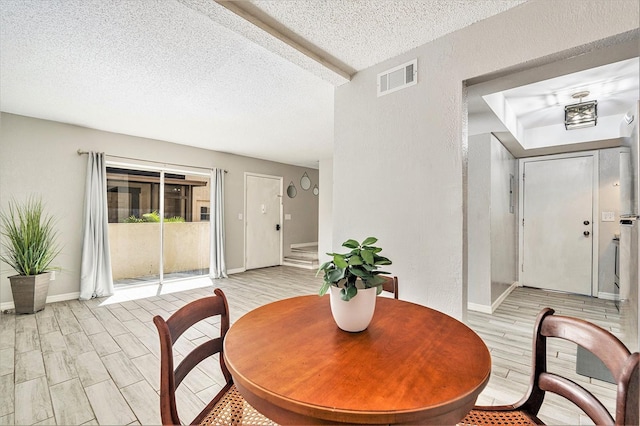 dining area with a textured ceiling, baseboards, visible vents, and wood finish floors