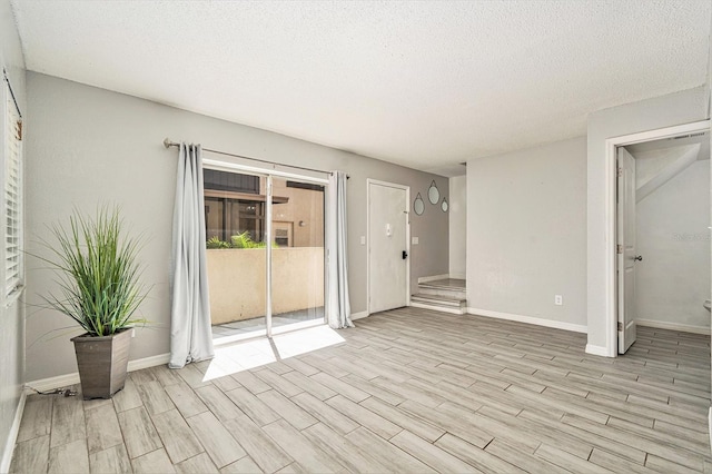 empty room with light wood finished floors, a textured ceiling, and baseboards