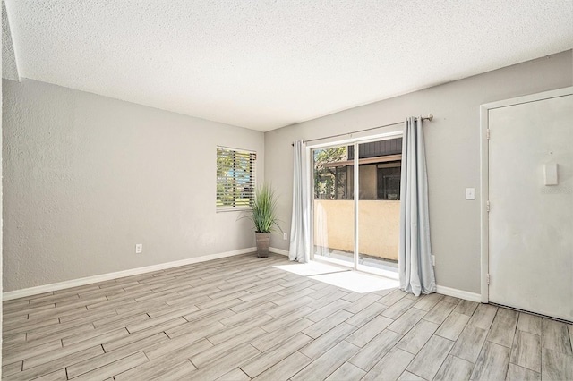 empty room with light wood-style flooring, a textured wall, baseboards, and a textured ceiling