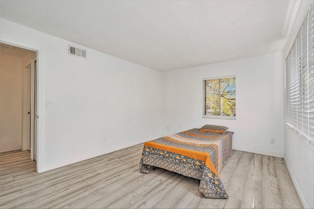 bedroom with visible vents, baseboards, a textured ceiling, and hardwood / wood-style floors