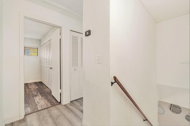 hallway with an upstairs landing, a textured ceiling, and wood finished floors