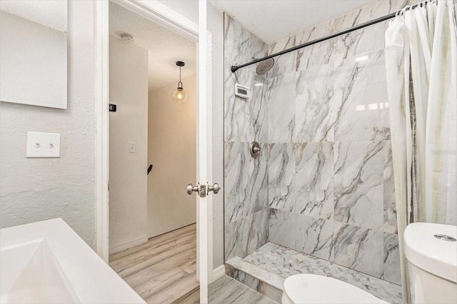 full bath with tiled shower, toilet, wood finished floors, and a textured ceiling