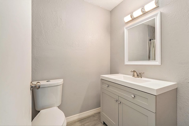 bathroom with toilet, vanity, baseboards, and wood finished floors