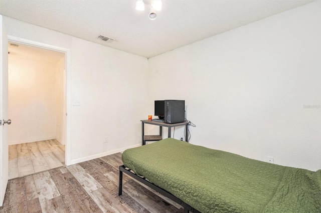 bedroom with visible vents, baseboards, a textured ceiling, and wood finished floors