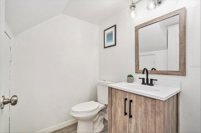 bathroom with baseboards, toilet, vaulted ceiling, wood finished floors, and vanity