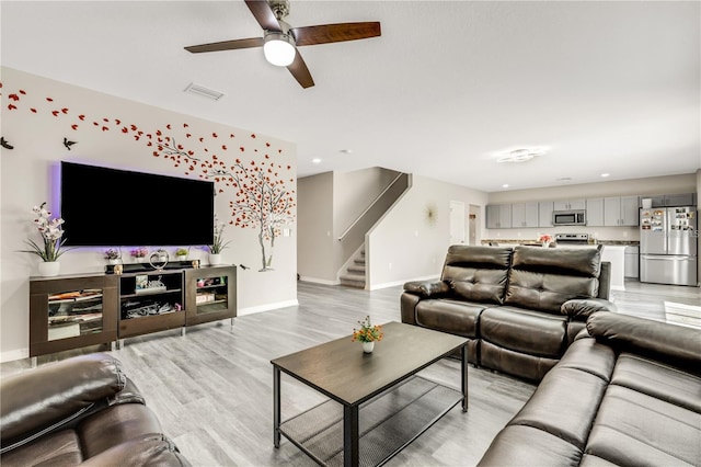 living area with visible vents, light wood-style flooring, stairway, ceiling fan, and baseboards