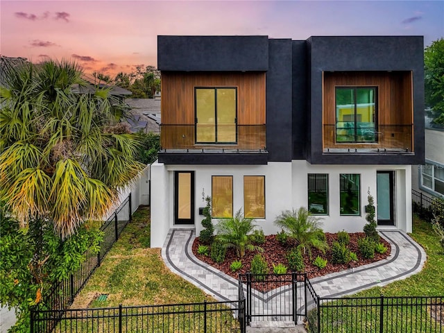 back of house at dusk featuring fence private yard, a gate, a lawn, and stucco siding