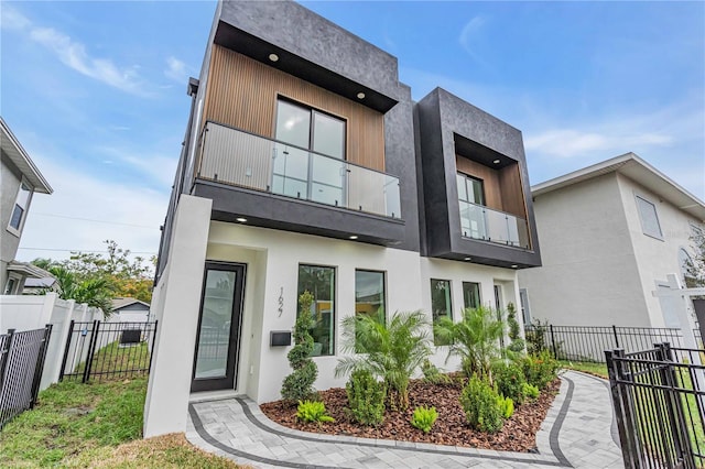 rear view of property featuring fence, a balcony, and stucco siding