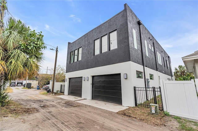 view of home's exterior featuring dirt driveway, fence, an attached garage, and stucco siding