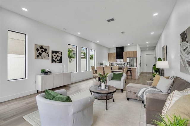 living area featuring baseboards, light wood finished floors, visible vents, and recessed lighting