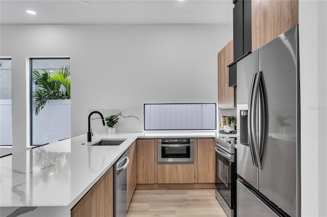 kitchen featuring light stone counters, light wood finished floors, stainless steel appliances, a sink, and modern cabinets