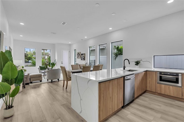 kitchen with appliances with stainless steel finishes, a sink, a peninsula, and light stone countertops