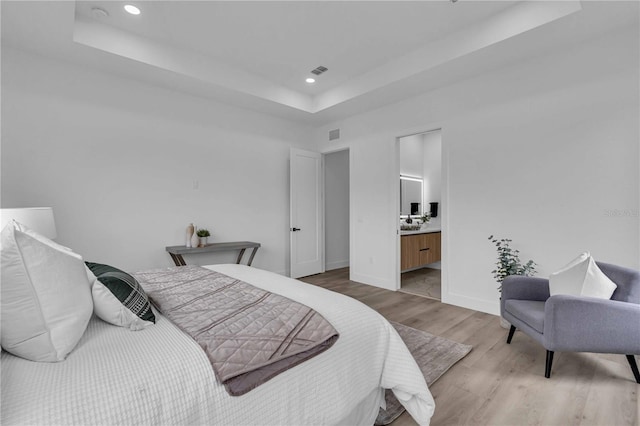 bedroom featuring baseboards, visible vents, a tray ceiling, light wood-style floors, and recessed lighting