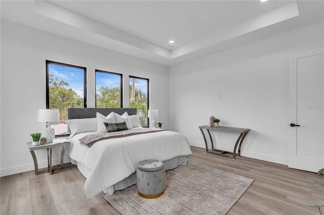 bedroom featuring light wood-type flooring, baseboards, a raised ceiling, and recessed lighting