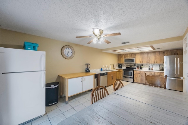 kitchen with brown cabinets, light tile patterned floors, stainless steel appliances, light countertops, and backsplash