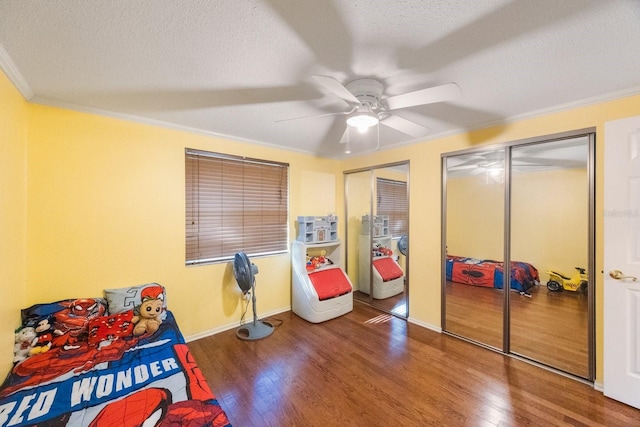 bedroom featuring dark wood-style floors, a textured ceiling, ornamental molding, and multiple closets