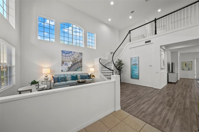 hall with visible vents, wood finished floors, recessed lighting, a towering ceiling, and stairs