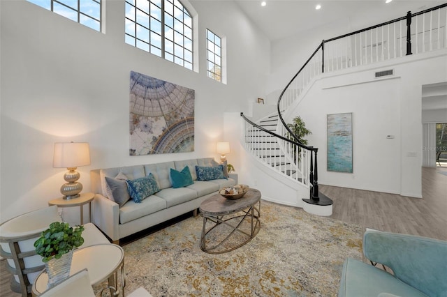 living area featuring visible vents, wood finished floors, recessed lighting, a towering ceiling, and stairs