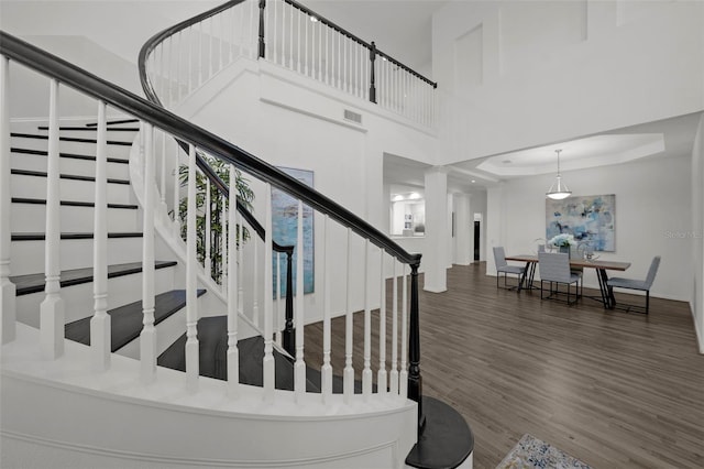 staircase with a tray ceiling, wood finished floors, visible vents, and a towering ceiling