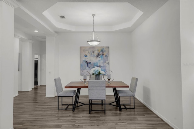 dining room with a tray ceiling, baseboards, visible vents, and wood finished floors