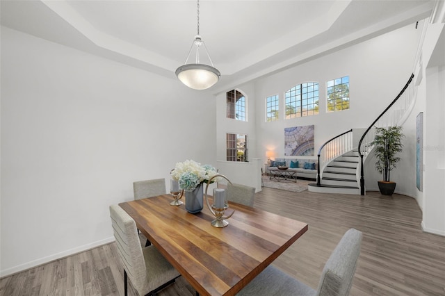 dining space with a tray ceiling, baseboards, stairs, and light wood finished floors