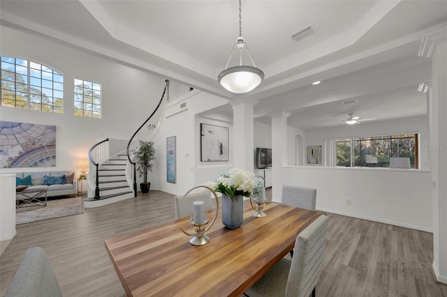 dining space with visible vents, a raised ceiling, wood finished floors, and ornate columns