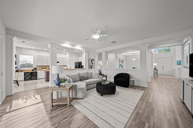 living area featuring a wealth of natural light, a ceiling fan, light wood-type flooring, and ornate columns