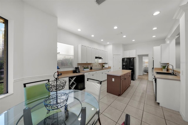 kitchen with black fridge, a sink, a center island, light tile patterned flooring, and light countertops