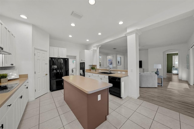 kitchen with a sink, black appliances, light tile patterned flooring, and a center island