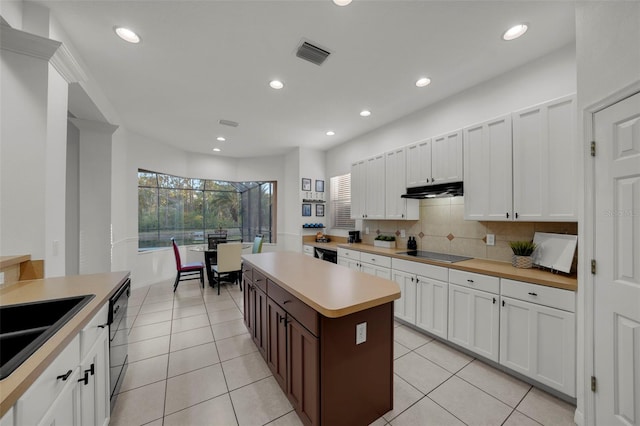 kitchen with visible vents, a kitchen island, black appliances, light countertops, and tasteful backsplash