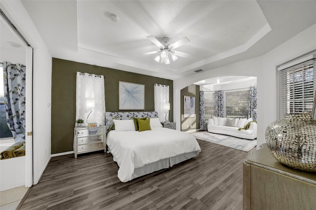 bedroom with arched walkways, visible vents, a raised ceiling, and wood finished floors