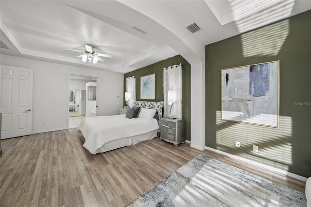 bedroom featuring visible vents, baseboards, a tray ceiling, and wood finished floors