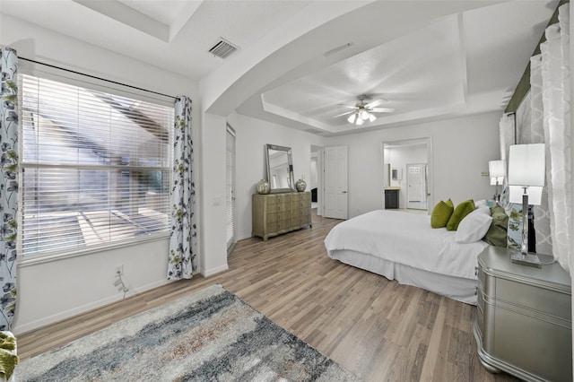 bedroom featuring visible vents, baseboards, wood finished floors, arched walkways, and a raised ceiling