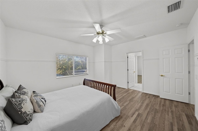 bedroom featuring a textured ceiling, wood finished floors, visible vents, and ceiling fan