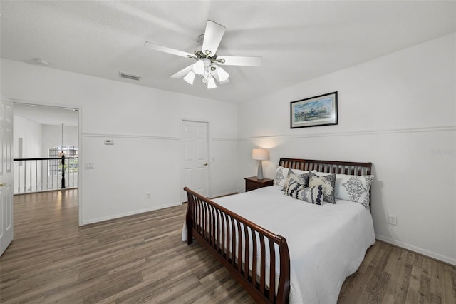 bedroom with a ceiling fan, wood finished floors, visible vents, and baseboards