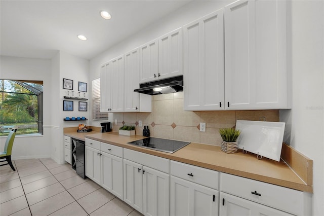 kitchen with black appliances, under cabinet range hood, light tile patterned floors, decorative backsplash, and white cabinetry